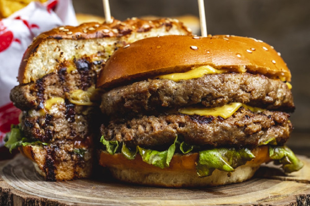 A double cheeseburger contains two grilled or fried flat round cakes of ground beef with cheese slices, filled in a roll or split bun with other toppings.